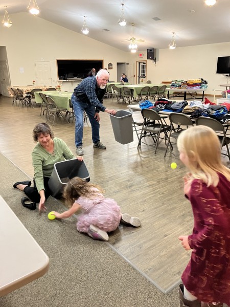 Girls playing a game with tennis balls and trashcans with a couple elder people